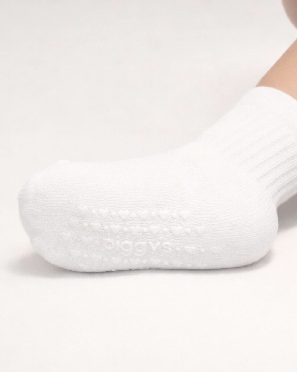 White baby crew sock with white silicone grips on an off-white background