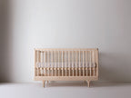 Caravan Crib in ash, mattress at the higher support height for newborns, mattress sitting mid-spindle.