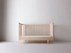 Caravan Crib in ash converted to three-walled toddler bed, front spindle rail removed, mattress in place.