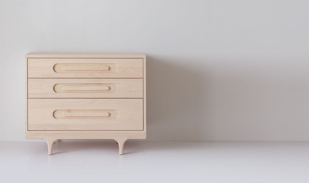 Caravan Dresser in ash, front view on a white studio floor, three drawers with oblong recessed pulls and sculpted legs.