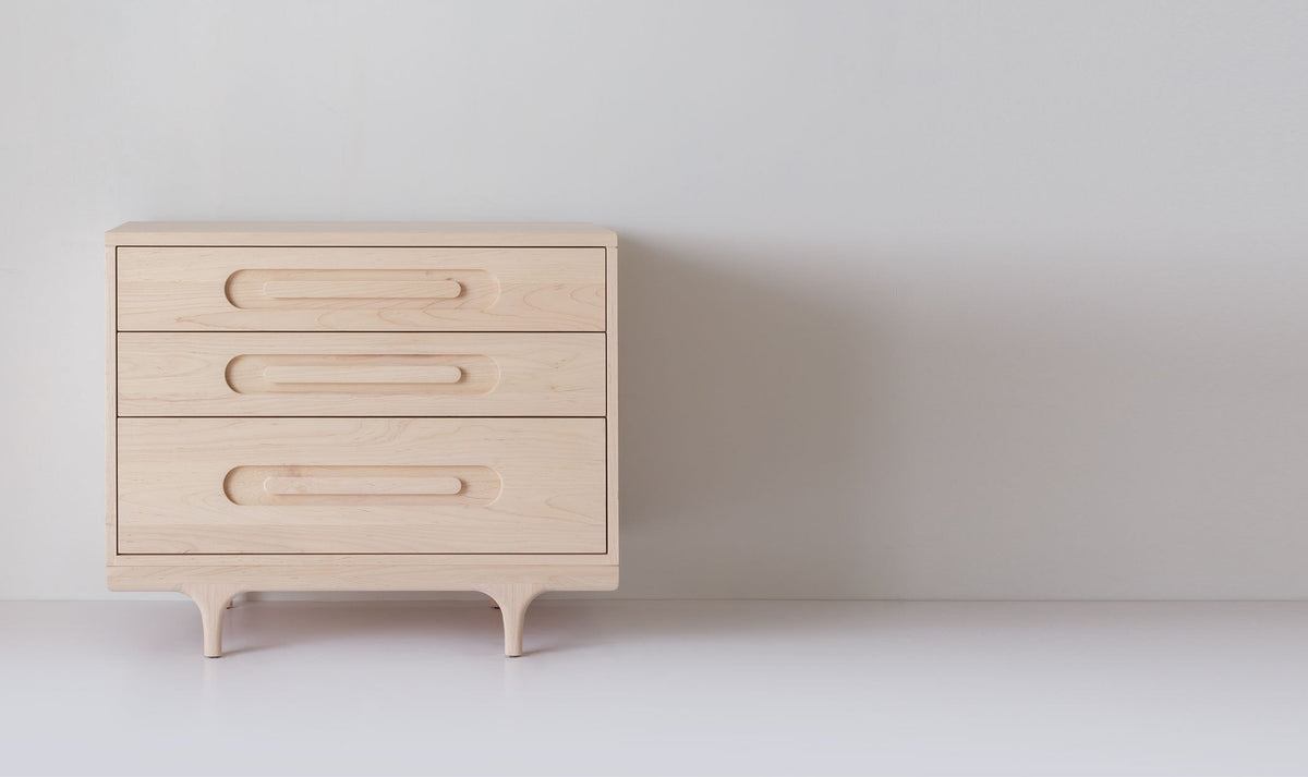 Caravan Dresser in ash, front view on a white studio floor, three drawers with oblong recessed pulls and sculpted legs.