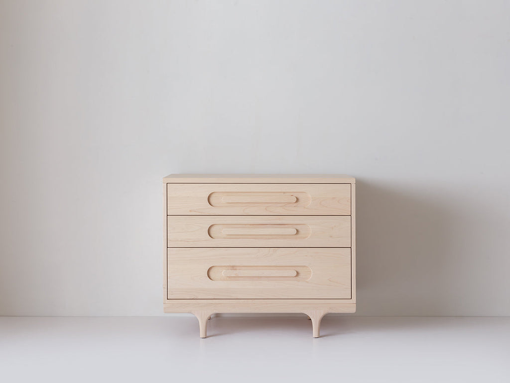 Caravan Dresser in ash, off-center front view on a white studio floor, three drawers with carved oblong recessed pulls.