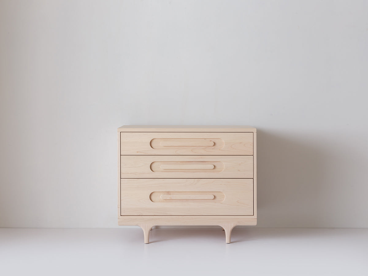 Caravan Dresser in ash, off-center front view on a white studio floor, three drawers with carved oblong recessed pulls.