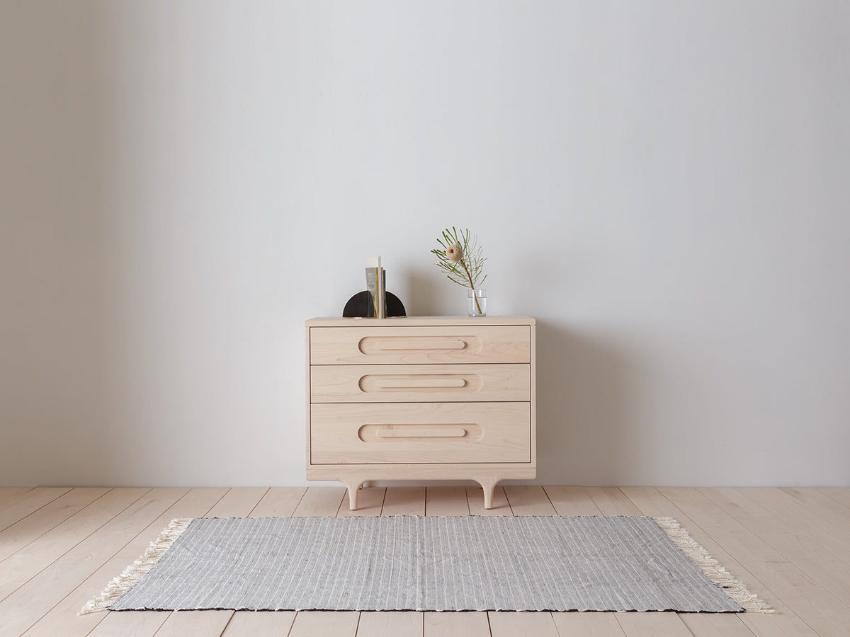 Caravan Dresser in ash on a maple plank floor with open book on a black bookend and a banksia branch in a glass vase on top.