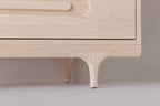 Caravan Dresser leg detail in ash, sculpted Crib-style leg meeting the base of the case on a white floor.
