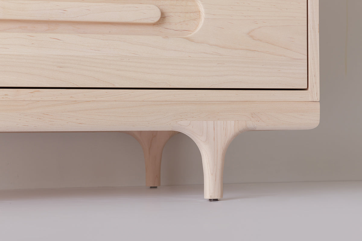 Caravan Dresser leg detail in ash, sculpted Crib-style leg meeting the base of the case on a white floor.