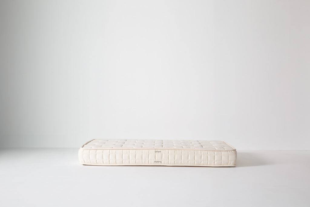 Dream No. 1 Mattress in cream organic cotton on a white studio floor, double-sided with Infant and Toddler labels visible.