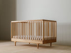 Caravan Crib in white oak with walnut corner caps, three-quarter view from above-front on a maple plank floor.