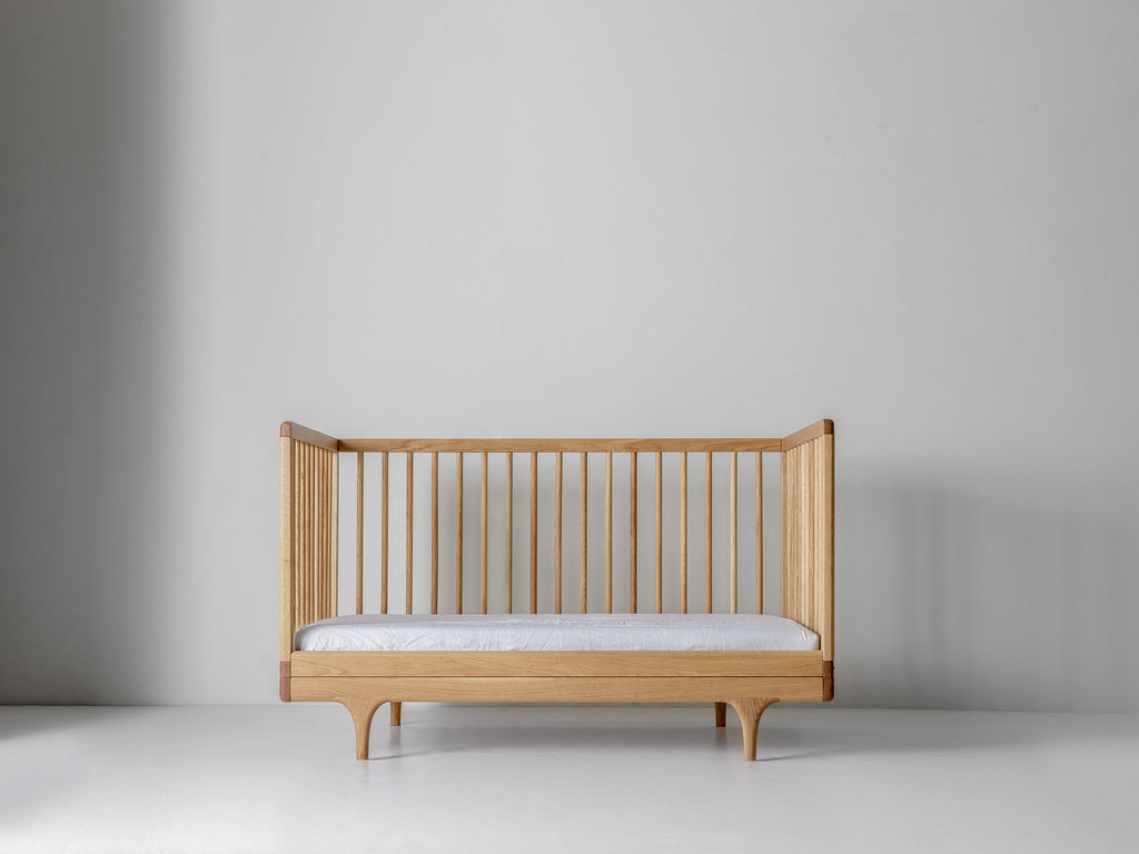 Caravan Crib in white oak with walnut caps, three-walled toddler bed conversion with mattress and front rail removed.