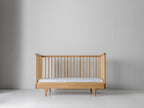 Caravan Crib in white oak with walnut caps, three-walled toddler bed conversion with mattress and front rail removed.