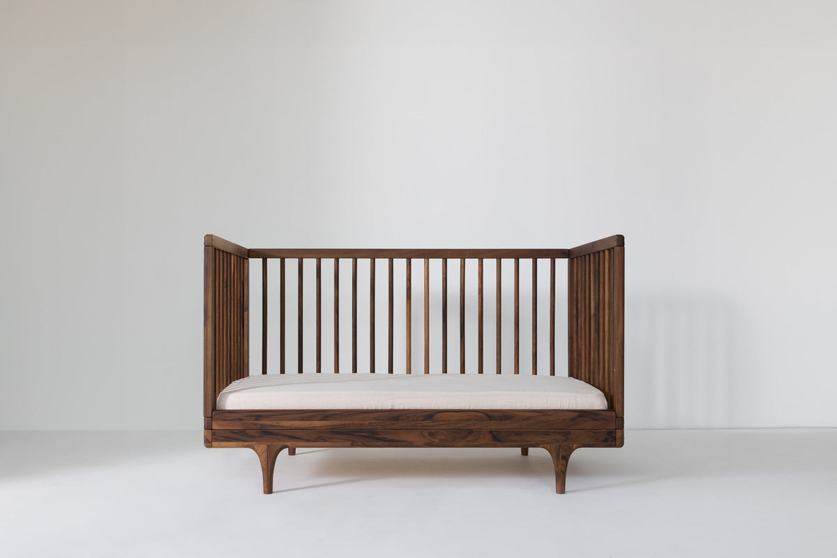 Caravan Crib in solid walnut converted to three-walled toddler bed, figured walnut grain across the base rail.