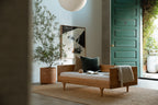Caravan Divan in white oak in a sunlit entryway with green paneled door, paper lantern, olive tree in terracotta pot.