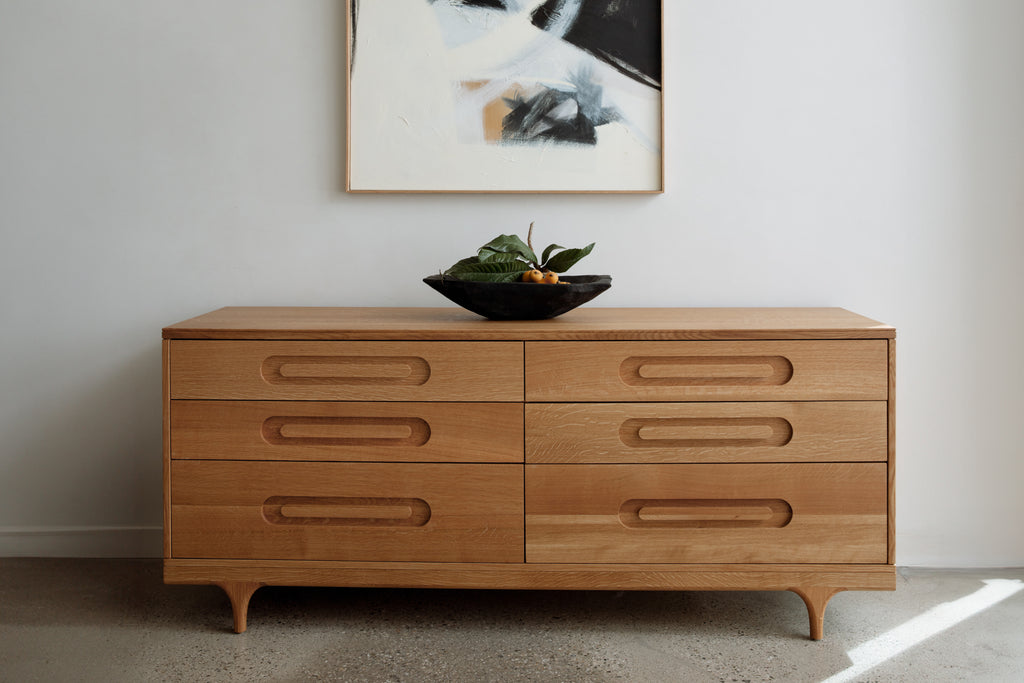 Caravan Double Dresser in white oak in a residential interior, black bowl with leaves and loquats, abstract painting above.