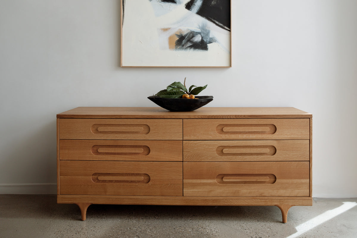 Caravan Double Dresser in white oak in a residential interior, black bowl with leaves and loquats, abstract painting above.