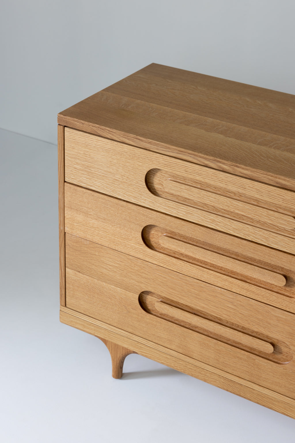 Caravan Dresser in white oak, three-quarter close-up showing the three drawers, oblong recessed pulls, and sculpted leg.