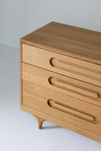 Caravan Dresser in white oak, three-quarter close-up showing the three drawers, oblong recessed pulls, and sculpted leg.