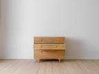 Caravan Dresser in white oak with the middle drawer pulled out, front view on a maple plank floor against a grey wall.