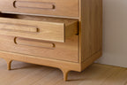 Caravan Dresser in white oak, three-quarter close-up with the middle drawer slid out, sculpted leg and recessed pulls.