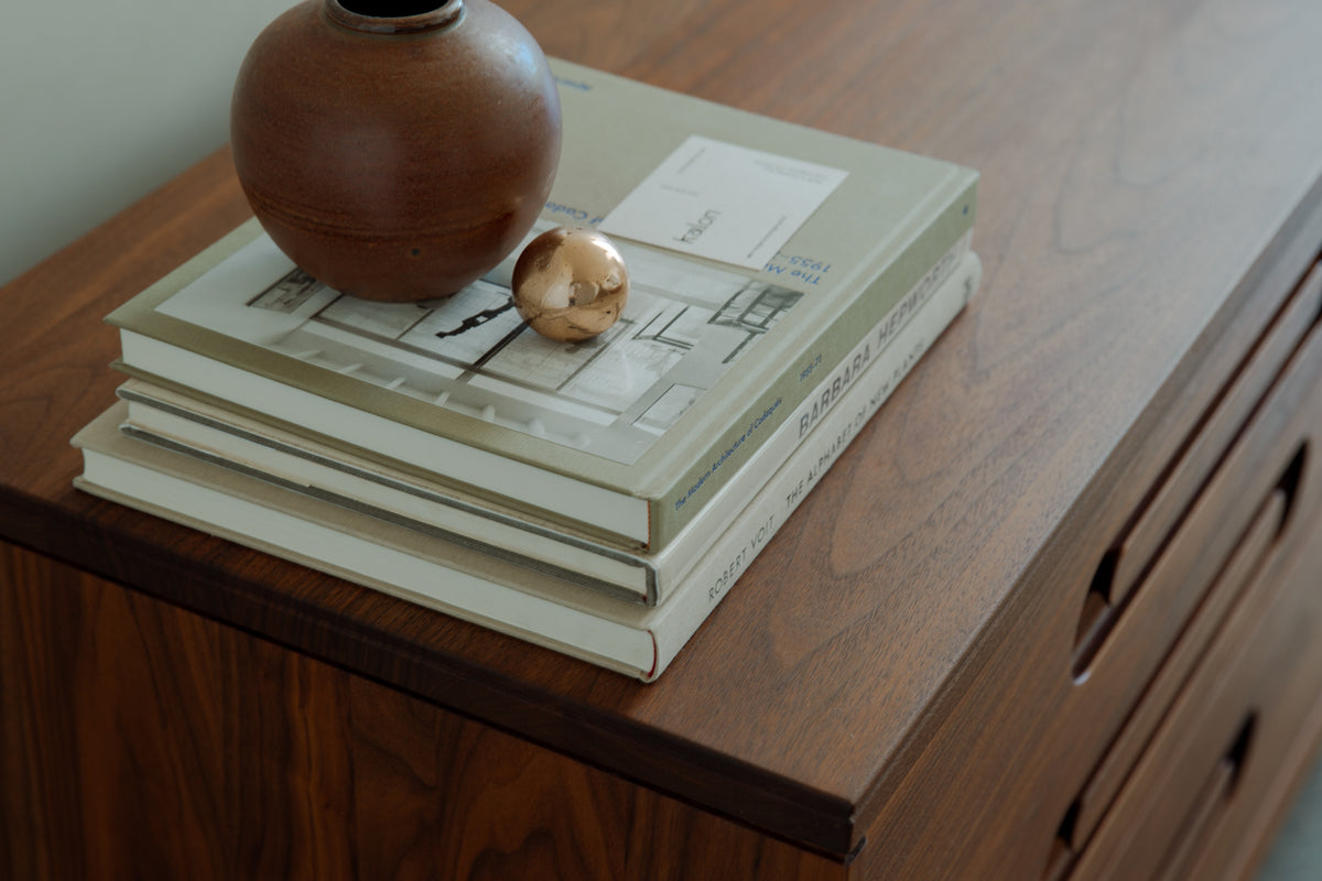 Caravan Double Dresser top in walnut with stacked Barbara Hepworth and Walker Evans books, terracotta vase, copper sphere.