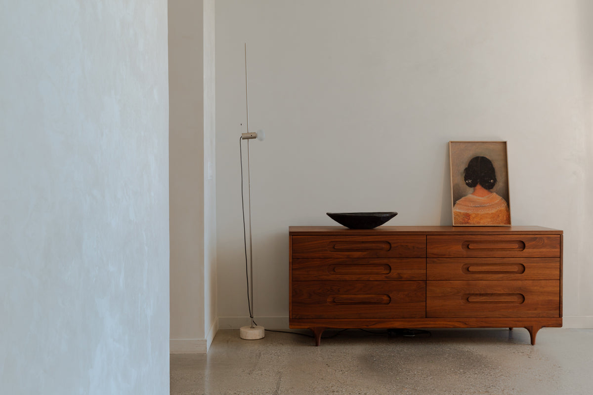 Caravan Double Dresser in walnut in a residential interior, dark shallow bowl and framed figurative portrait propped on top.
