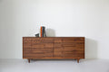Caravan Double Dresser in walnut with stacked Pierre Yovanovitch design books and a small dark stone sculpture as bookend.