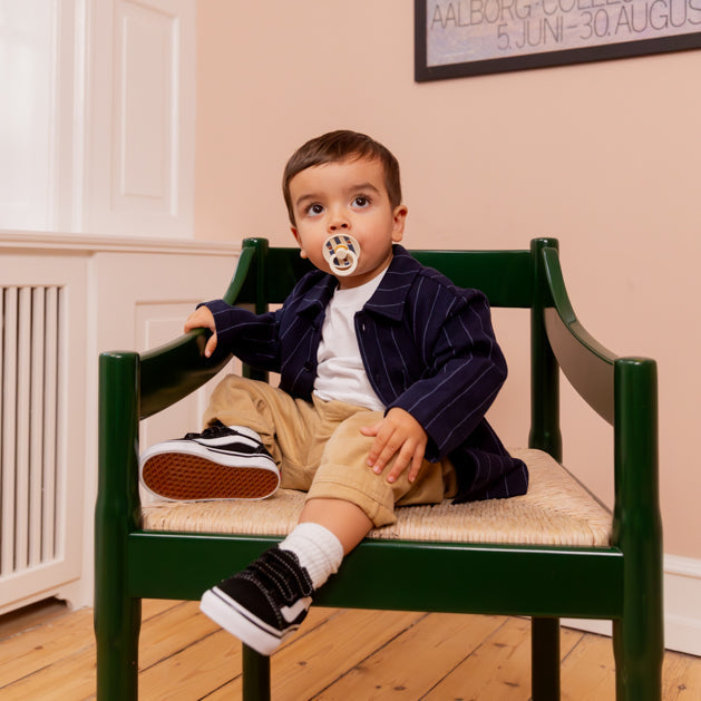 Toddler with a BIBS pacifier sitting in a green wooden chair