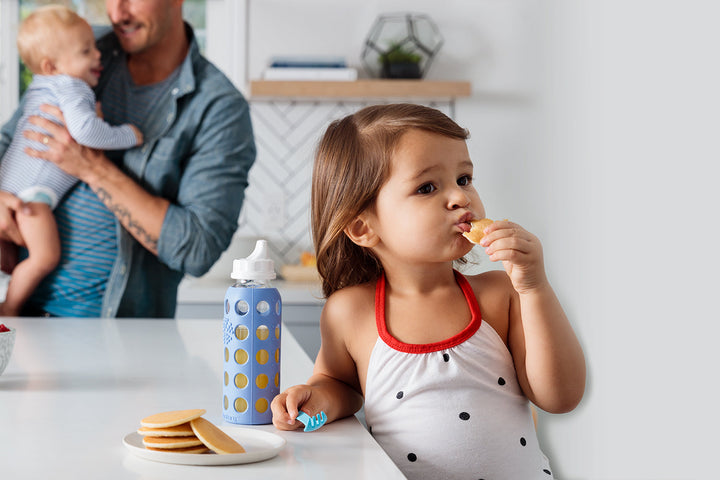 Toddler drinking from a Lifefactory glass bottle at a kitchen counter