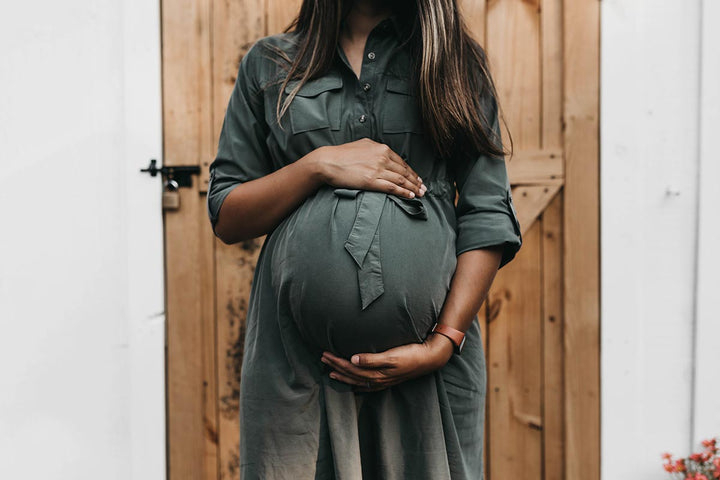 Pregnant woman in a green shirt dress holding her belly