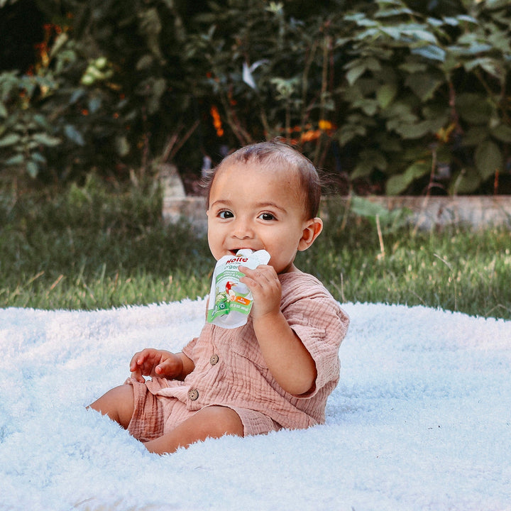 Baby on a blanket eating from a Holle organic yogurt pouch