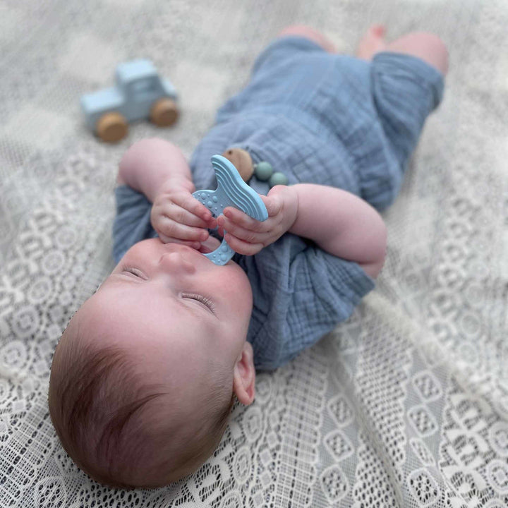 Baby holding a Hevea fish teether while lying on a blanket