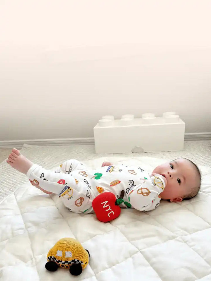 Estella — Baby lying on a white mattress with toys, wearing a patterned onesie.