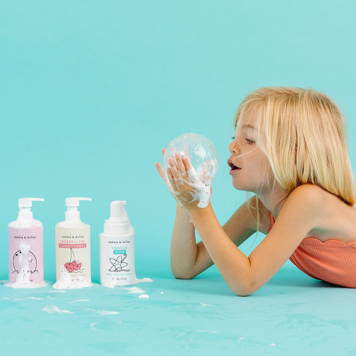 Girl blowing bubbles beside Dabble & Dollop bath products