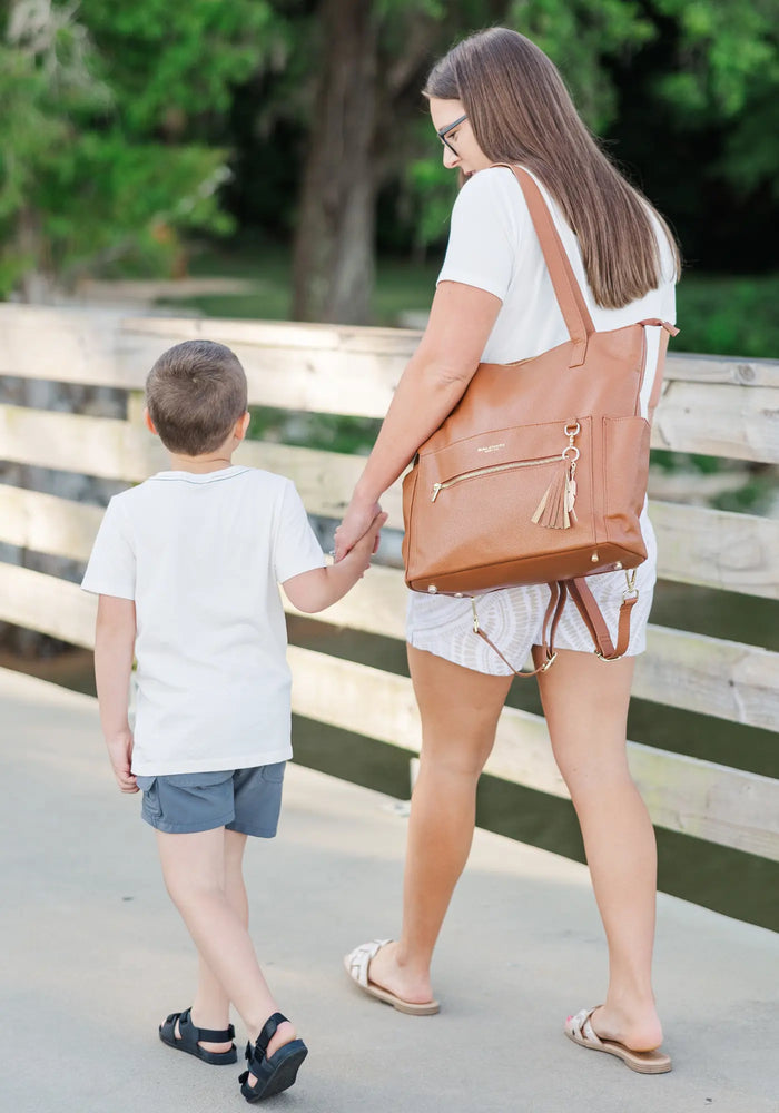 Baldwin Baby Company — Woman with brown diaper bag holding hands with a young boy on a wooden walkway outdoors.