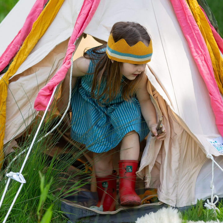 Girl in a Little Green Radicals striped pinafore crawling out of a tent