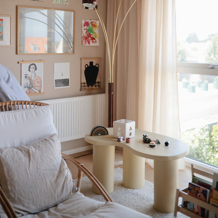Mushie — A cozy living room with a modern beige coffee table, rattan armchair, light curtains, and framed art