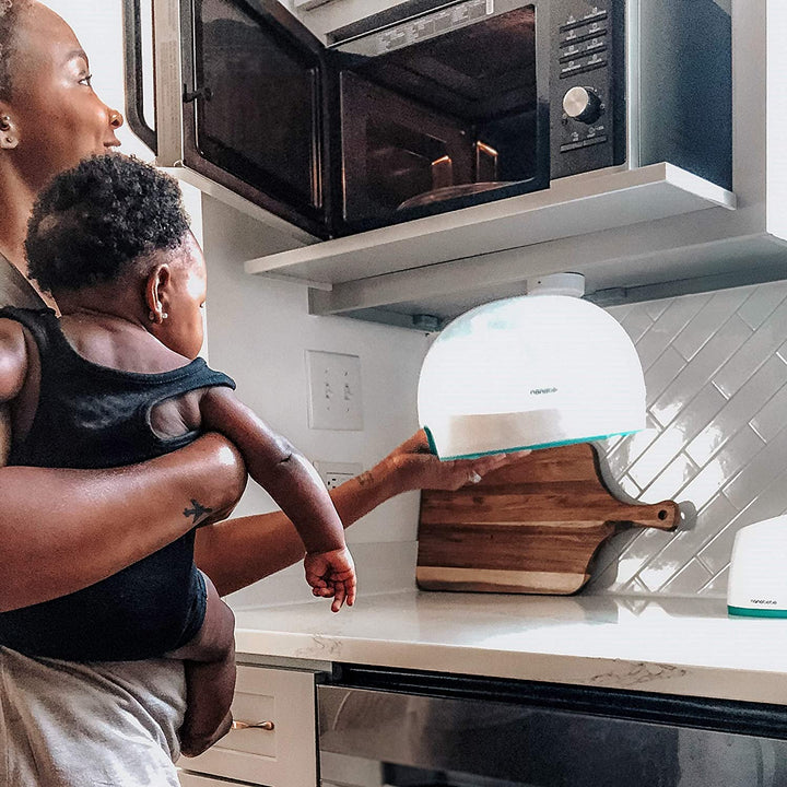 Parent holding a baby while using the Nanobébé microwave steam sterilizer