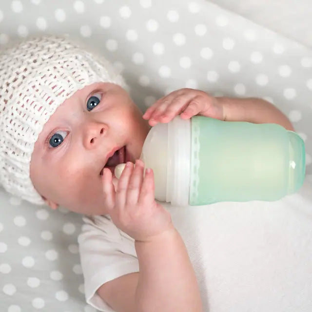Olababy — A newborn in a knitted bonnet lying on a spotted blanket, one hand resting on a mint silicone Gentle