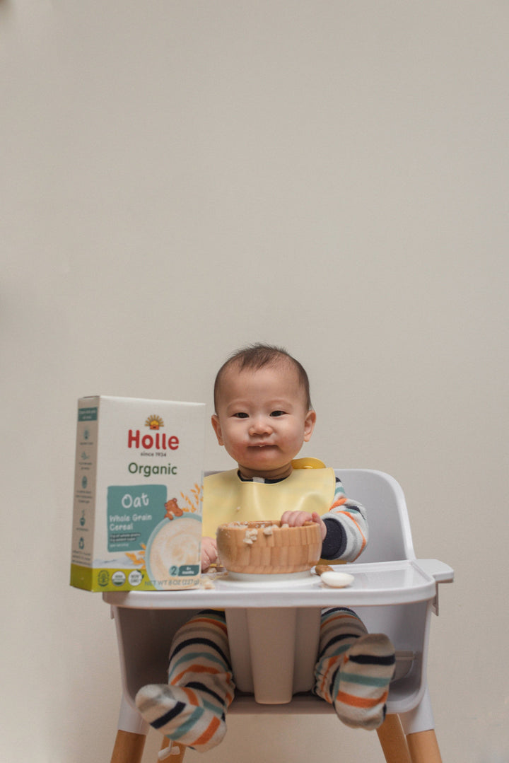 Baby in a high chair with a box of Holle organic oat cereal