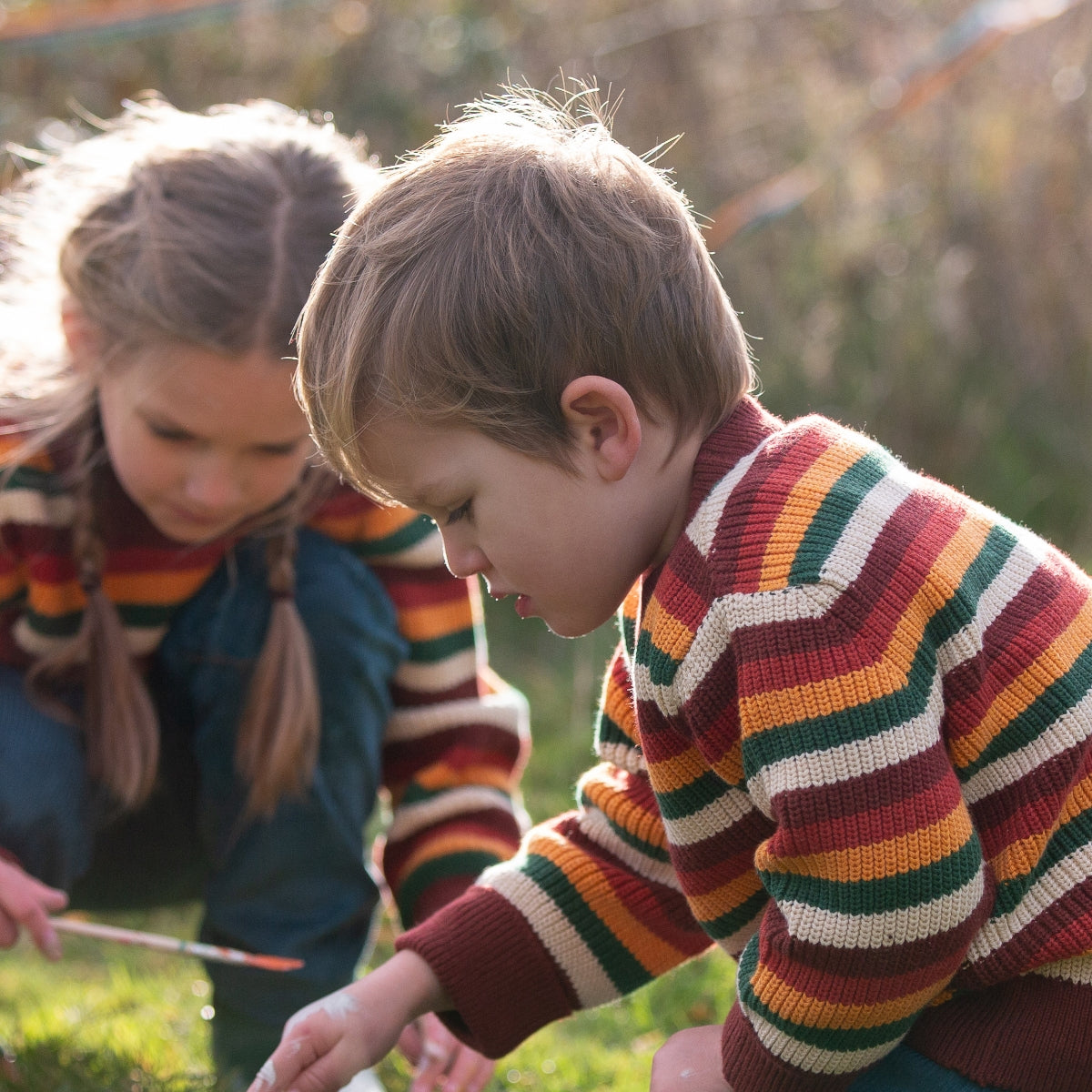 Two children in Little Green Radicals rainbow striped jumpers playing outdoors