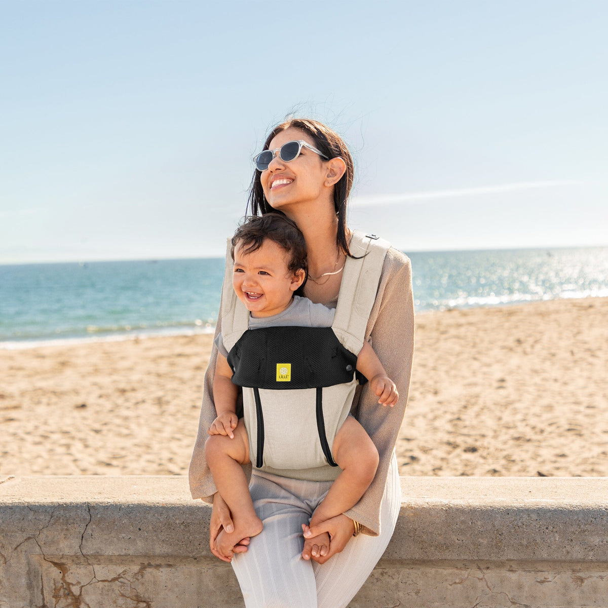 Mother on a beach carrying her baby in a LÍLLÉbaby carrier