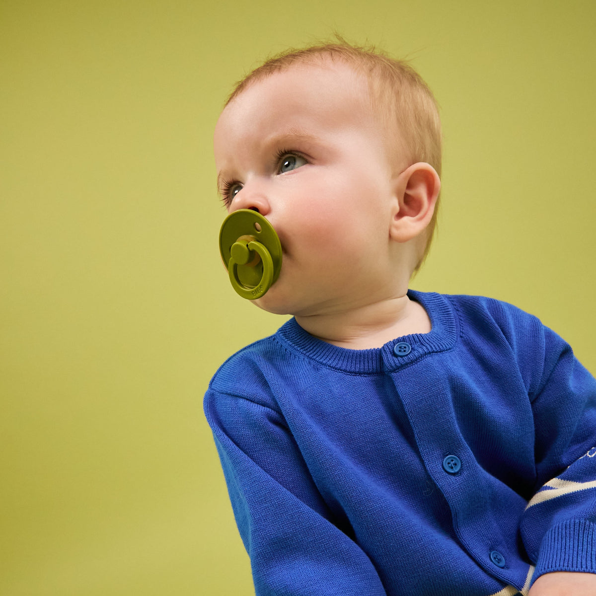 Baby with a BIBS Colour pacifier against a yellow-green backdrop