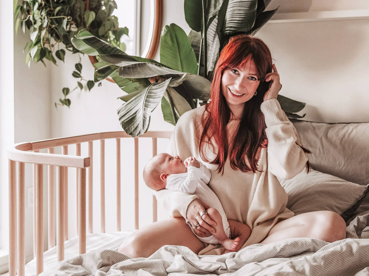 Mother holding her newborn beside a babybay bedside co-sleeper