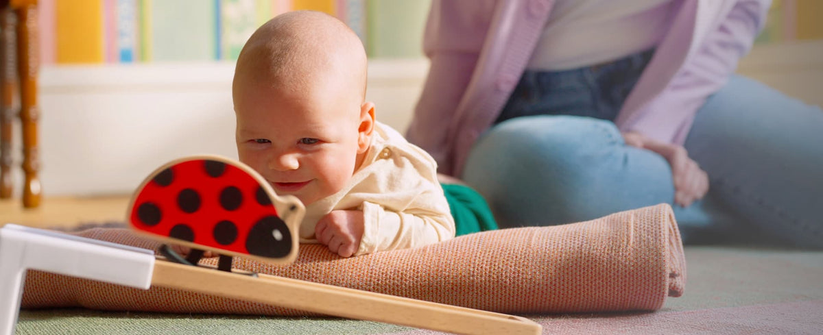 Baby on their tummy smiling at a wooden ladybug toy from a Lovevery Play Kit