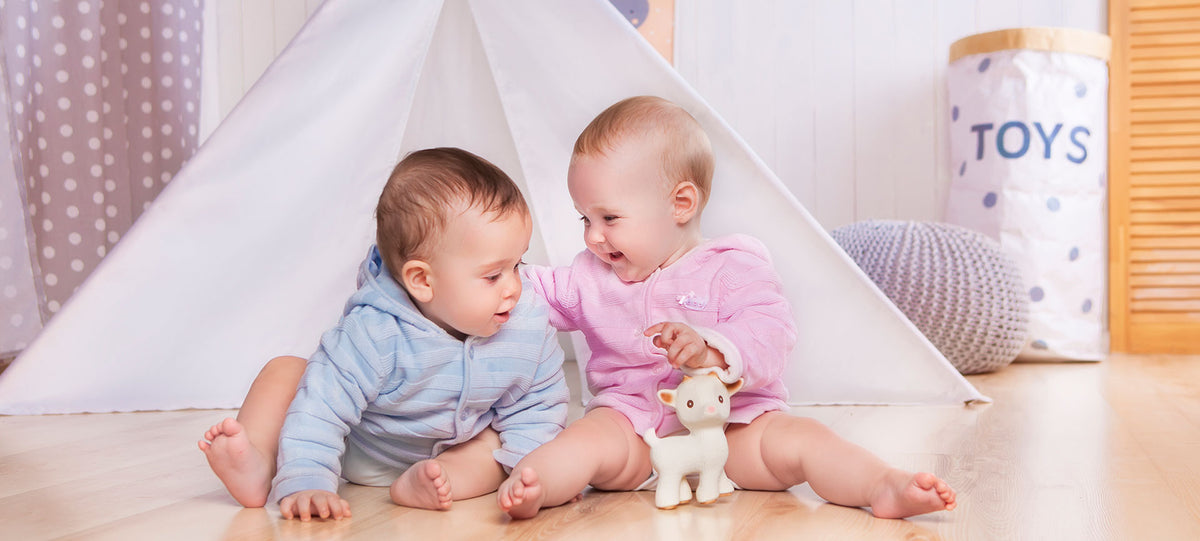 Two babies playing with a CaaOcho natural rubber lamb toy