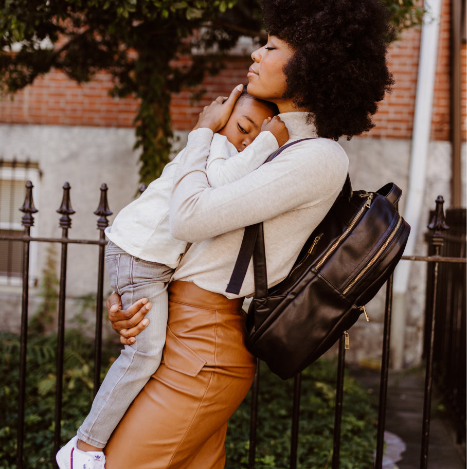 Mother hugging her child while wearing a Fawn Design diaper bag backpack