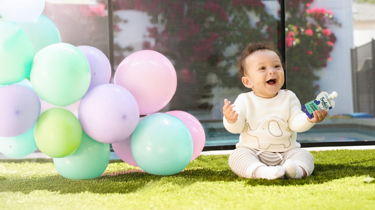 Sophie's Organics — Happy baby holding Sophie's Organics Berry Cool organic baby food pouch outdoors with balloons. 