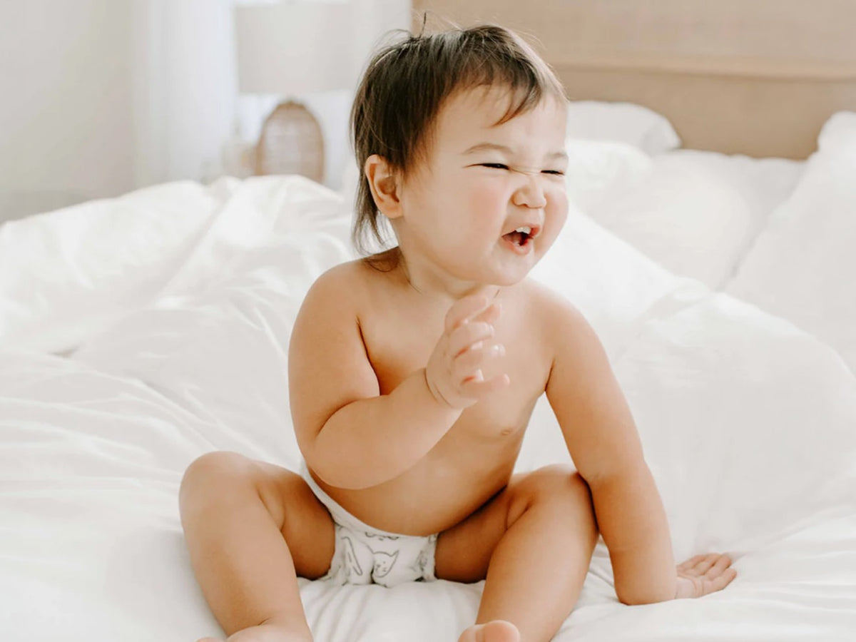 Laughing baby in a Parasol diaper sitting on a white bed